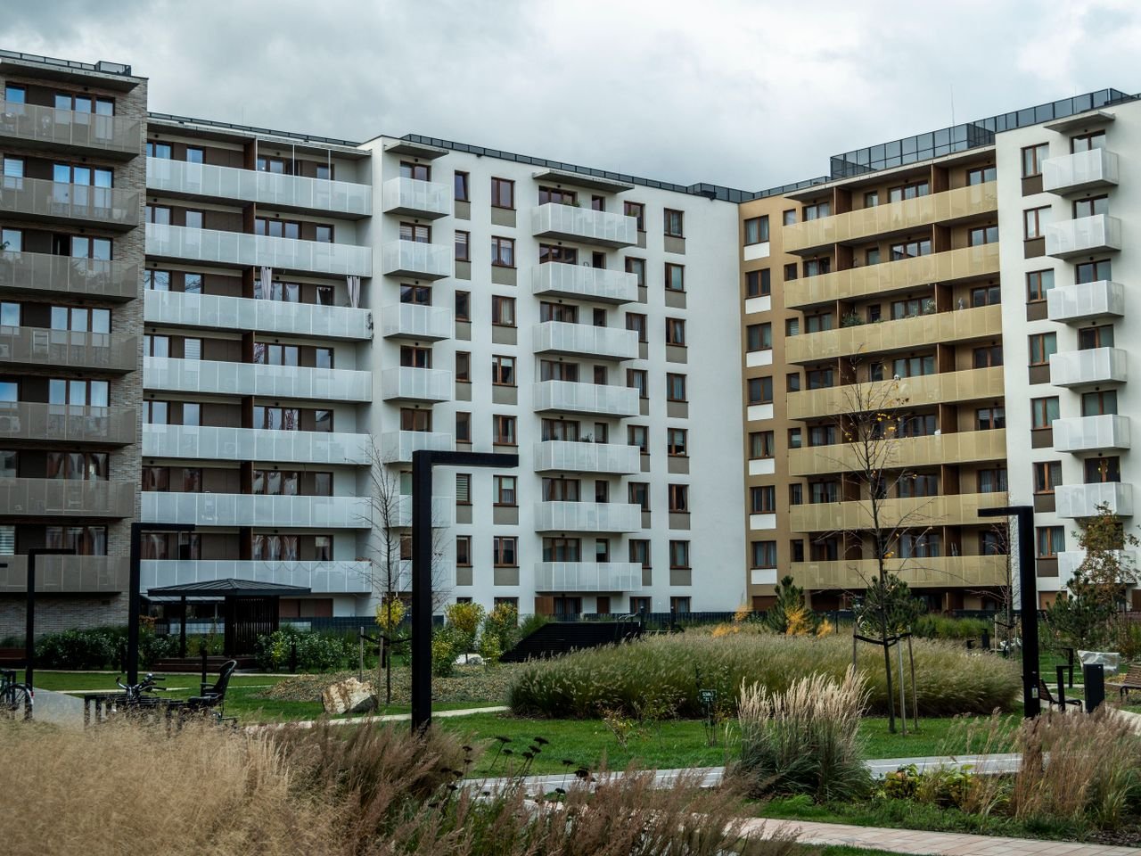A modern apartment building surrounded by landscaped greenery under a cloudy sky.