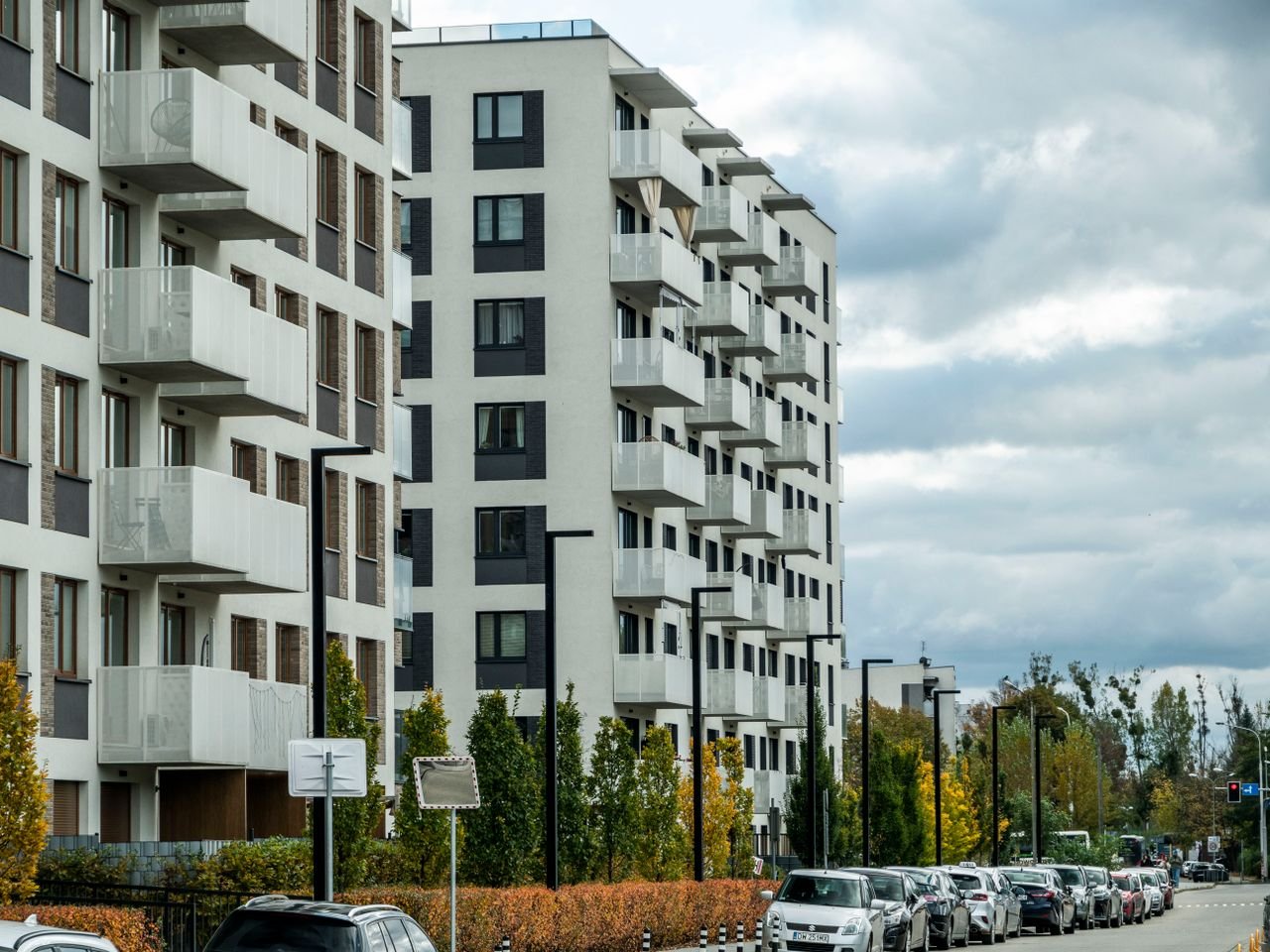 creative-02 Contemporary apartment complex on a city street lined with parked cars and autumn foliage.