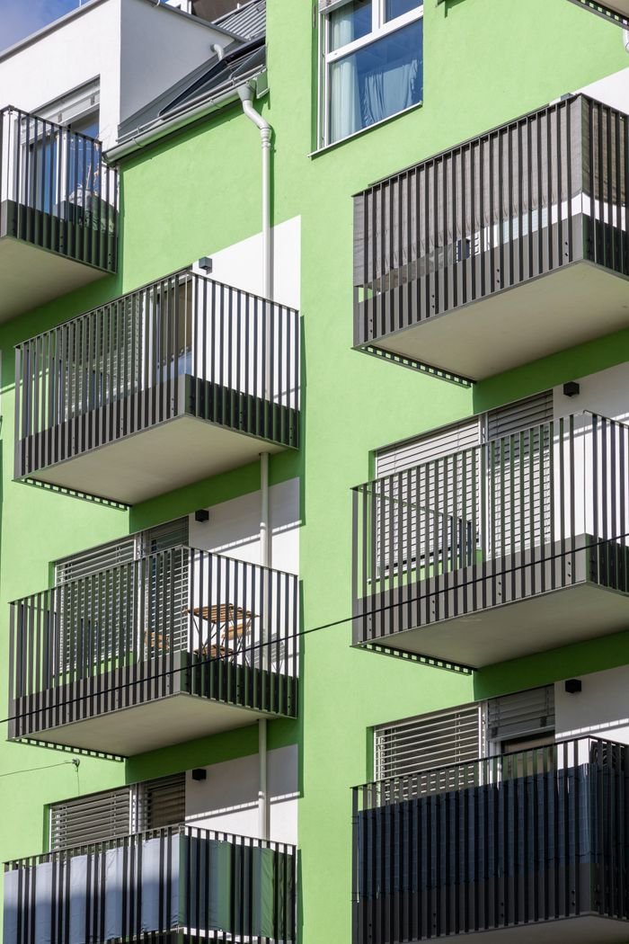mobile-02 Contemporary apartment building with green facade and multiple balconies under daytime light.