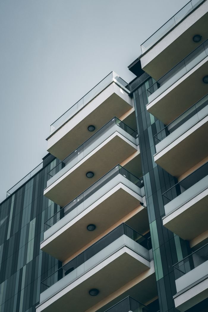 From below facade of contemporary building with geometric pattern and glass balconies against cloudless blue sky